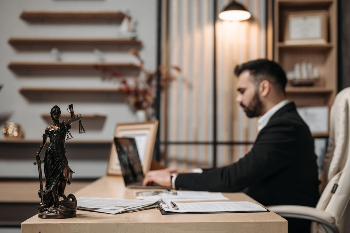 A lawyer working through documents at a laptop, with a figure of Lady Justice on the desk
